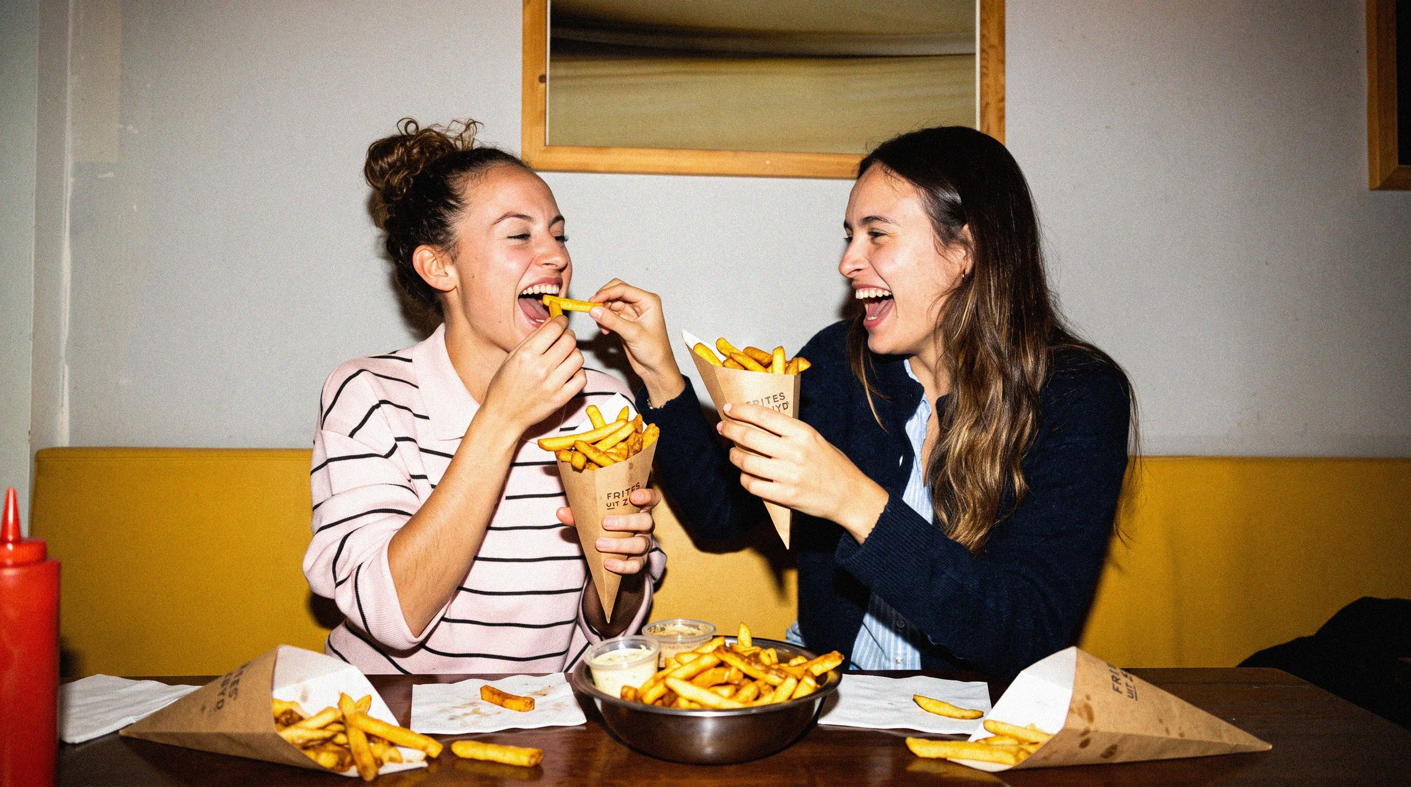 Twee vriendinnen lachen en delen een puntzak verse frites